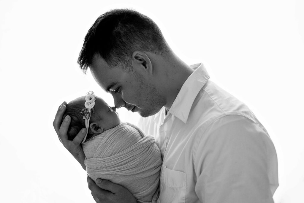 proud father touching noses with swaddled newborn baby girl