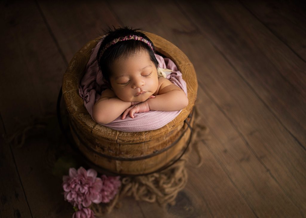 newborn baby girl posed in honey bucket with pink flowers