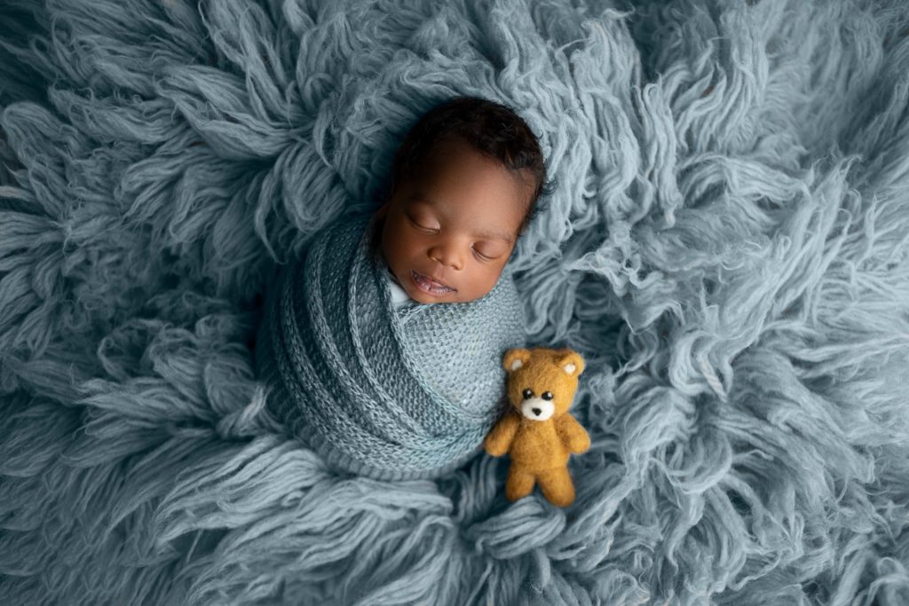 smiling newborn baby boy swaddled in blue wrap