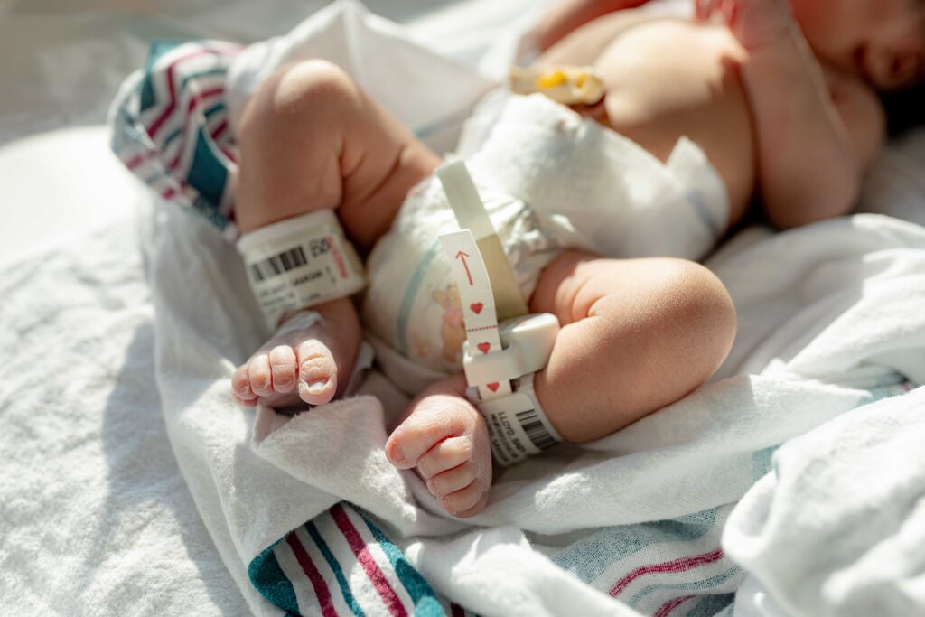 Close-up of a newborn's tiny feet with hospital ID bands, captured during a Fresh 48 session. Natural light highlights the delicate details of the baby’s first hours